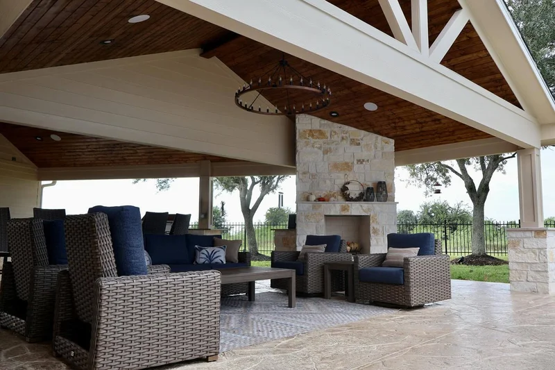 Covered patio with vaulted wood ceiling, stone fireplace, chandelier, and wicker furniture with blue cushions in Houston