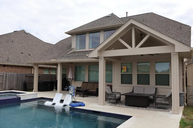 Pool and covered patio with gable roof, exposed trusses and outdoor seating in Houston neighborhood