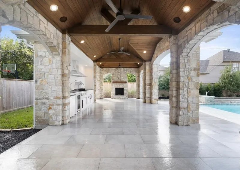 Grand covered patio with stone arch columns, wood ceiling, outdoor kitchen and pool view