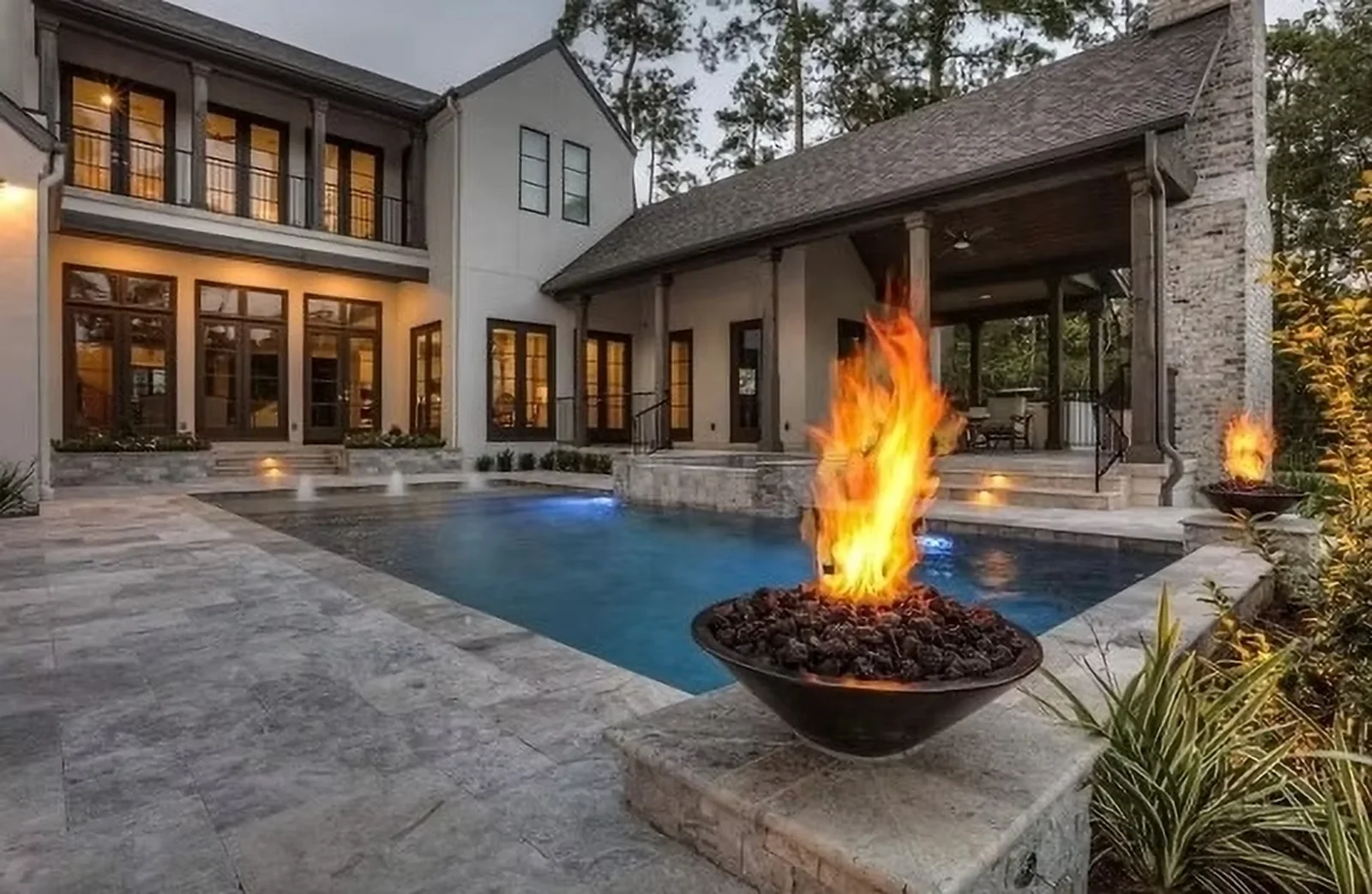 Luxury backyard with pool, fire bowls, and covered patio at dusk in Houston